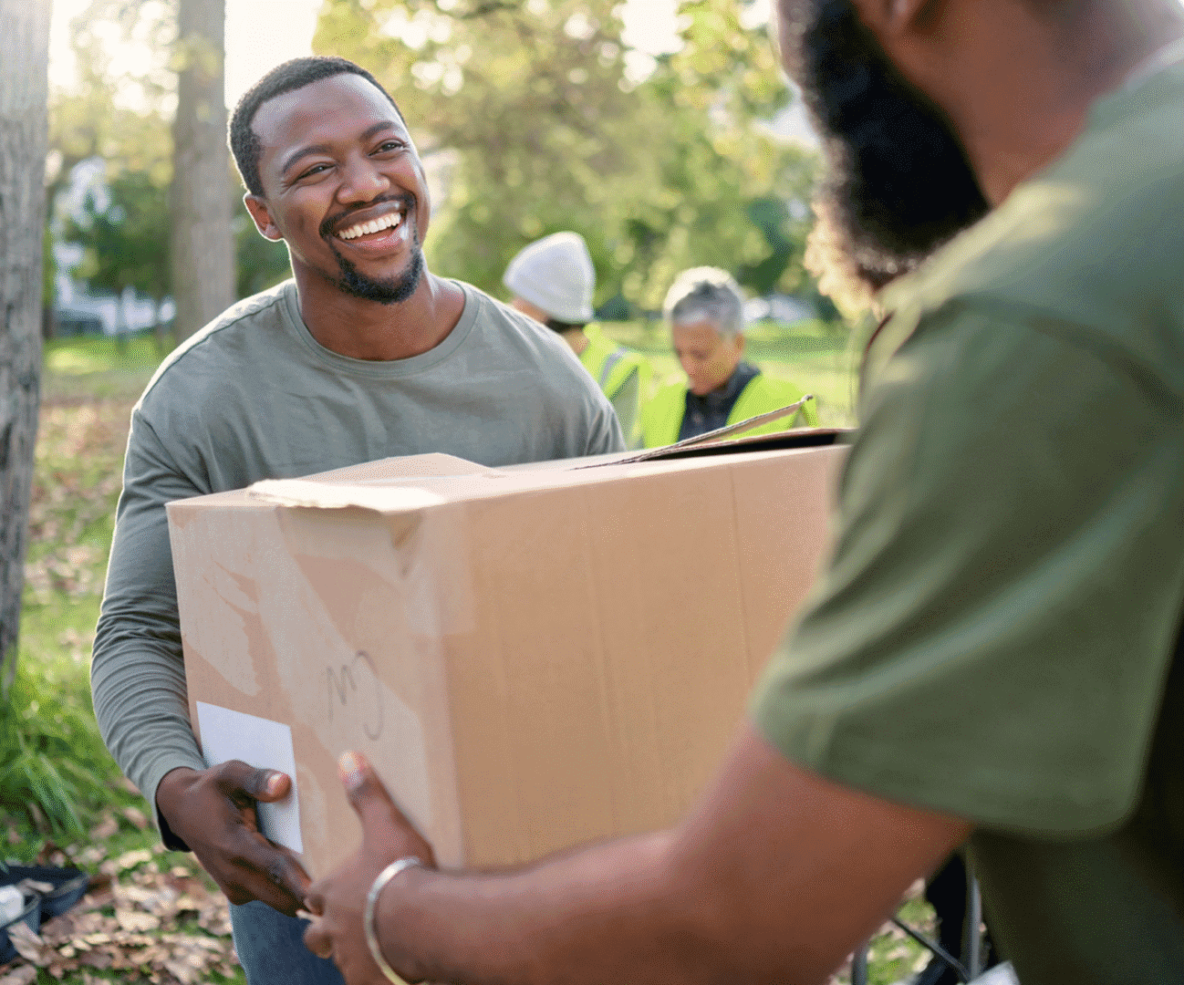 People exchanging a cardboard box outdoors.