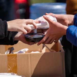 Hands exchanging packaged food at distribution event.