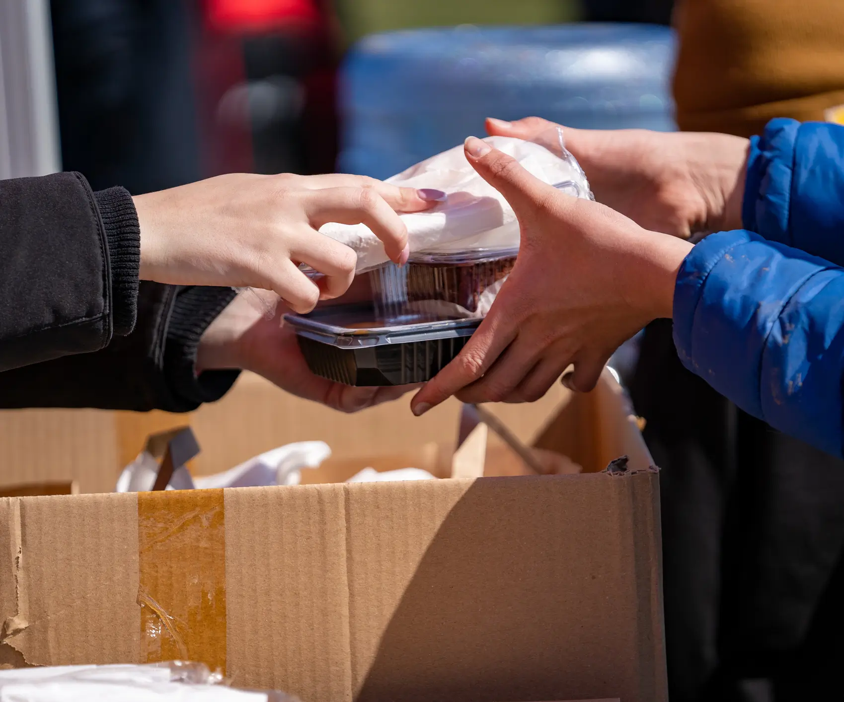 Hands exchanging packaged food at distribution event.