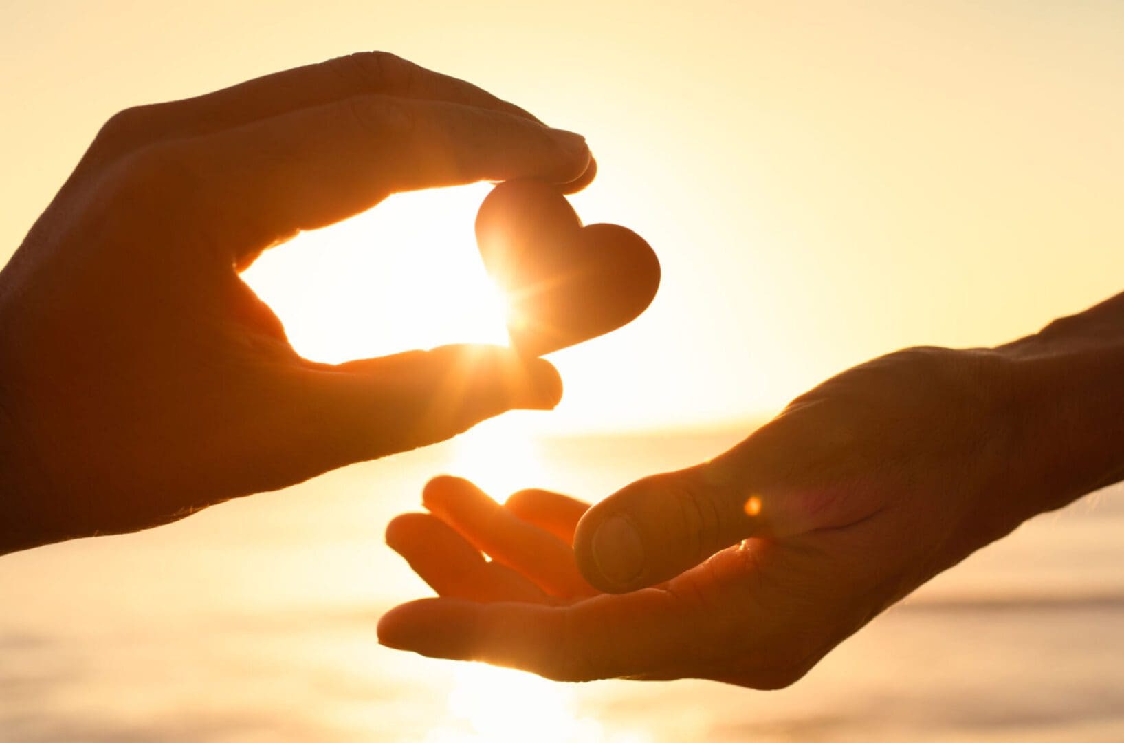Hands exchanging heart against sunset background.