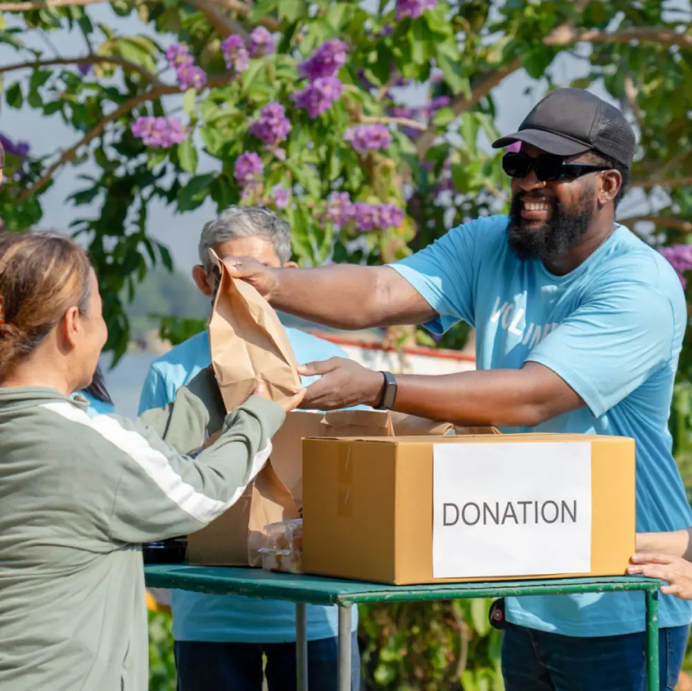 People distributing donations outdoors near flowers.