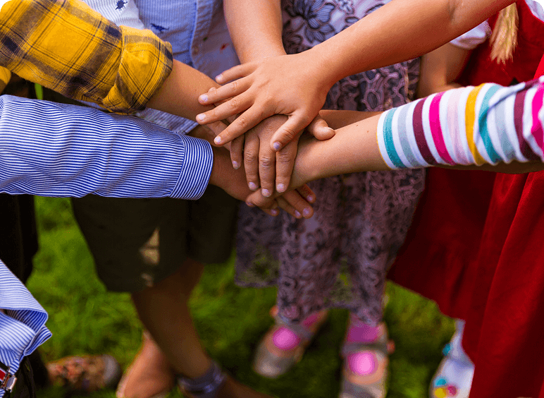 Children's hands stacked in unity outdoors.