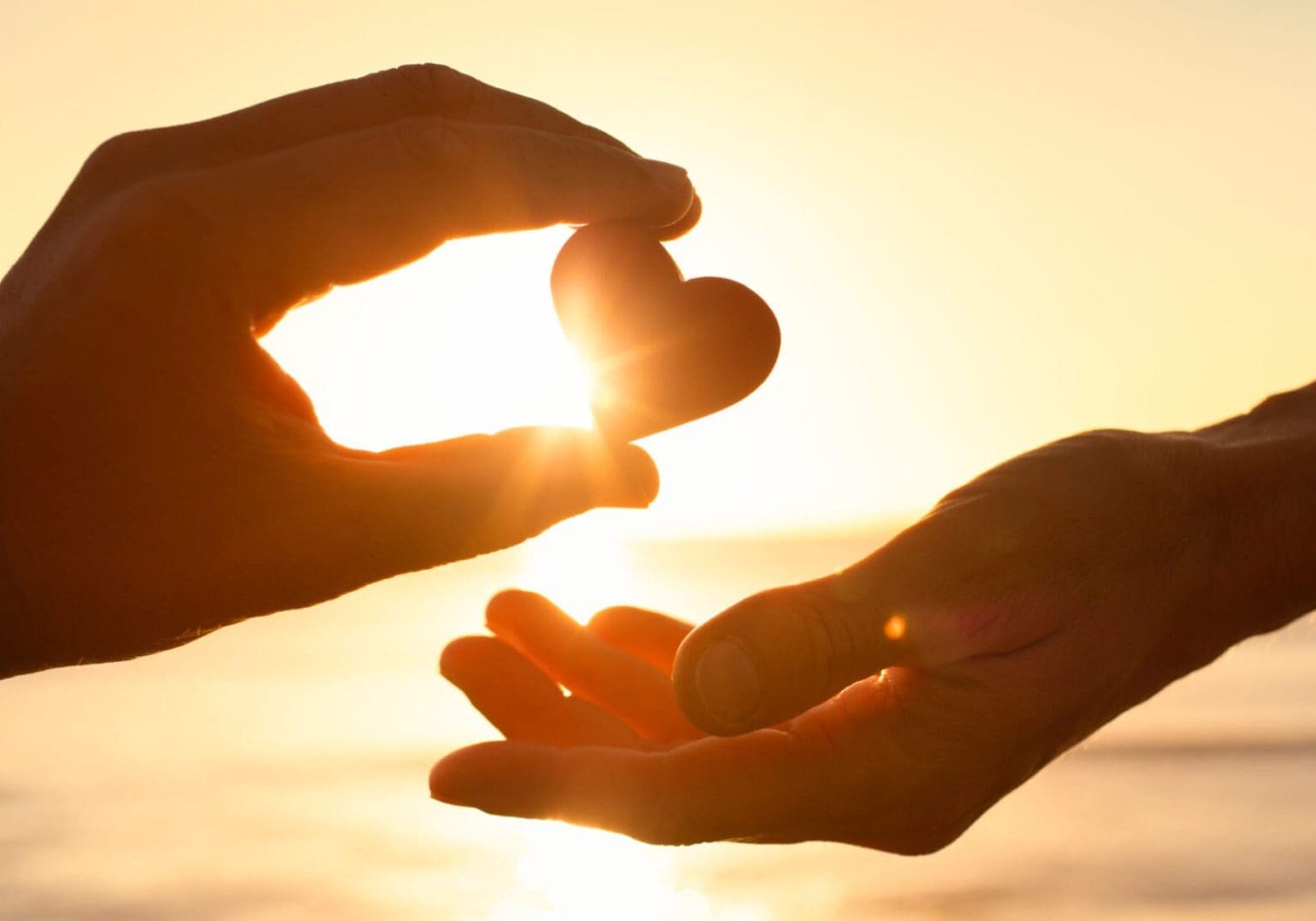 Hands exchanging heart against sunset background.